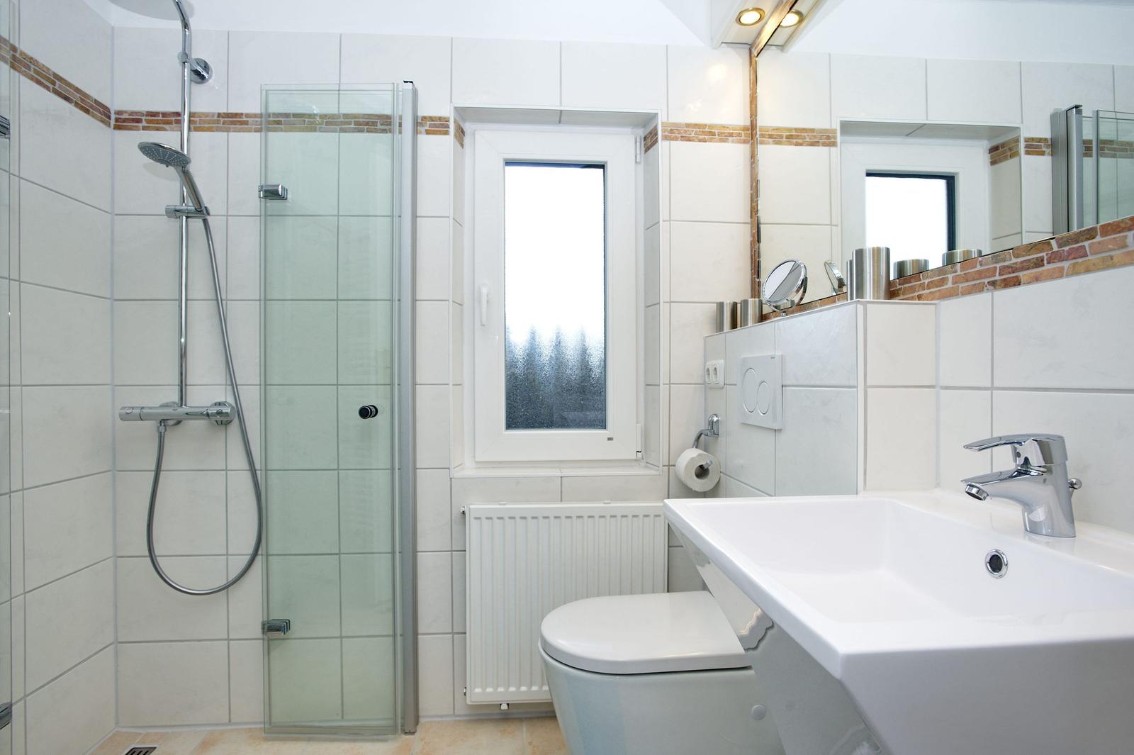 Badezimmer mit Dusche, Waschbecken und Toilette. Fenster mit Blick nach draußen.