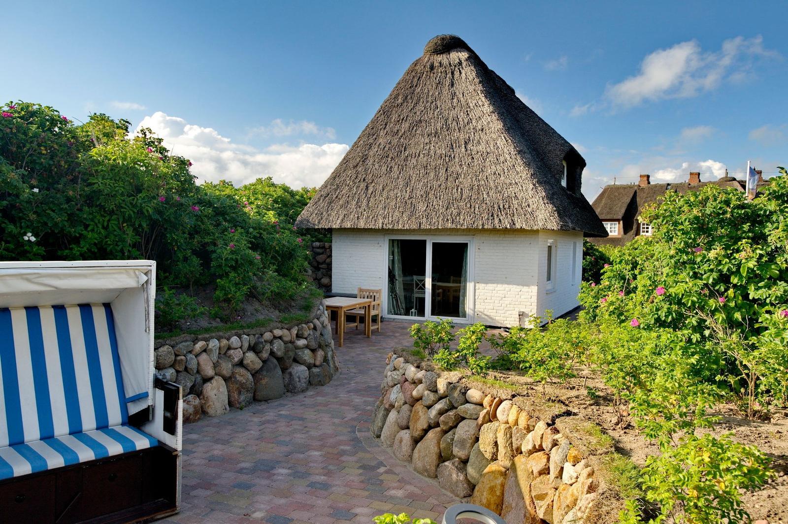 Hütte mit Strohdach, Garten, Terrasse und Strandliege.