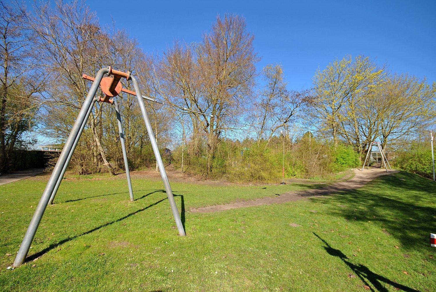 Ein Spielplatz mit Schaukel und Grünfläche unter blauem Himmel.