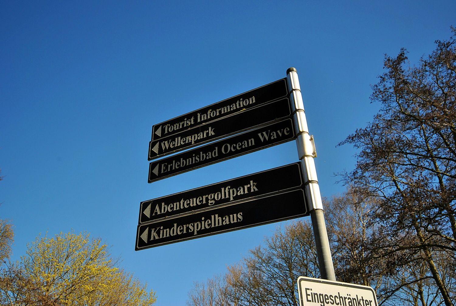 Schild weist auf Touristeninformation, Wellenpark, Erlebnisbad Ocean Wave, Abenteuergolfpark und Kinderspielhaus.