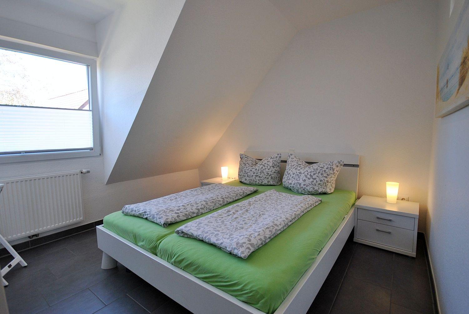Schlafzimmer mit Doppelbett, grüner Bettwäsche und zwei Nachttischen mit Lampen.