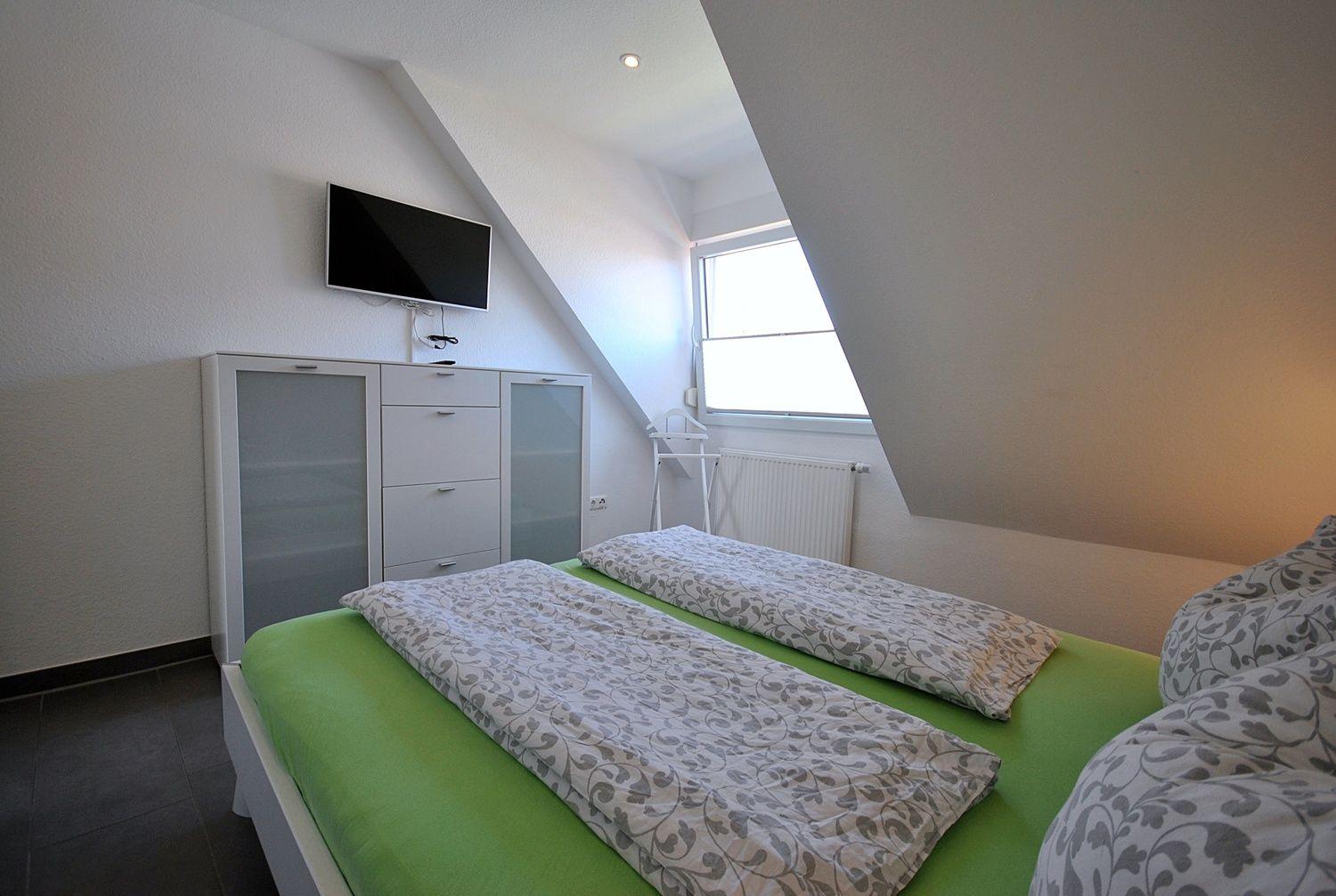 Schlafzimmer mit Doppelbett, TV und Fenster unter Dachschrägen.