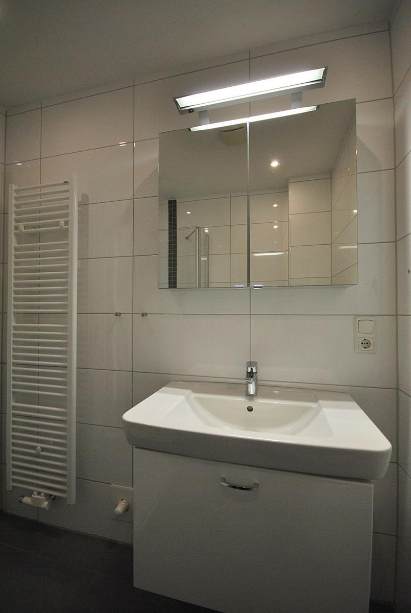 Badezimmer mit Waschbecken, Spiegel und Heizkörper an der Wand.