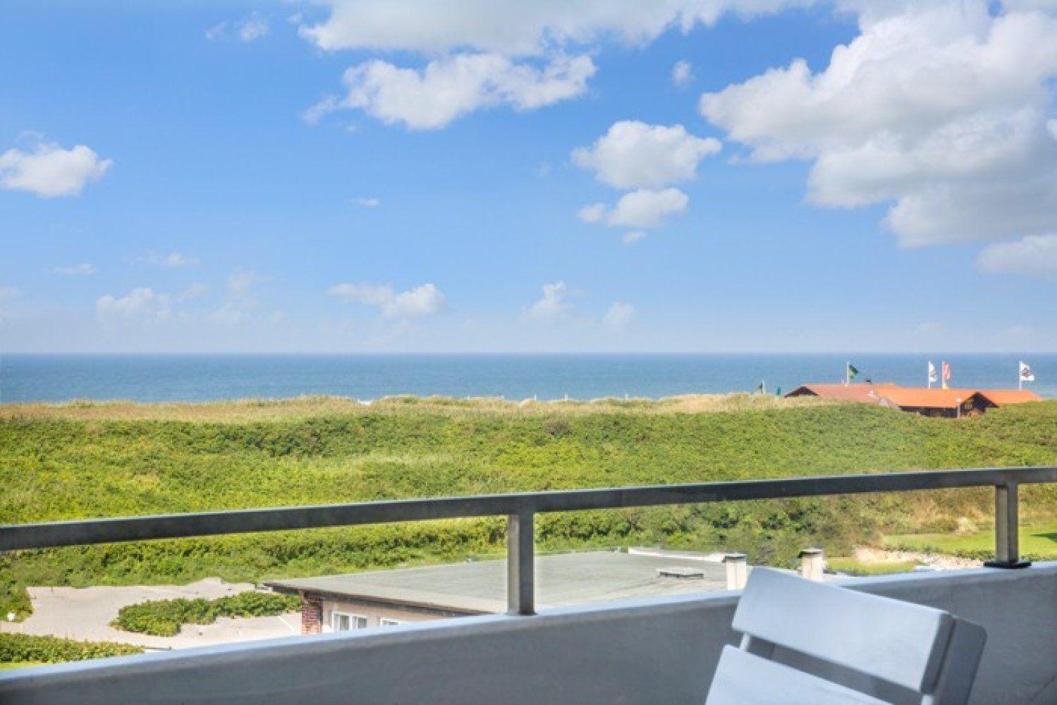 Balkon mit Blick auf das Meer und grüne Dünen.