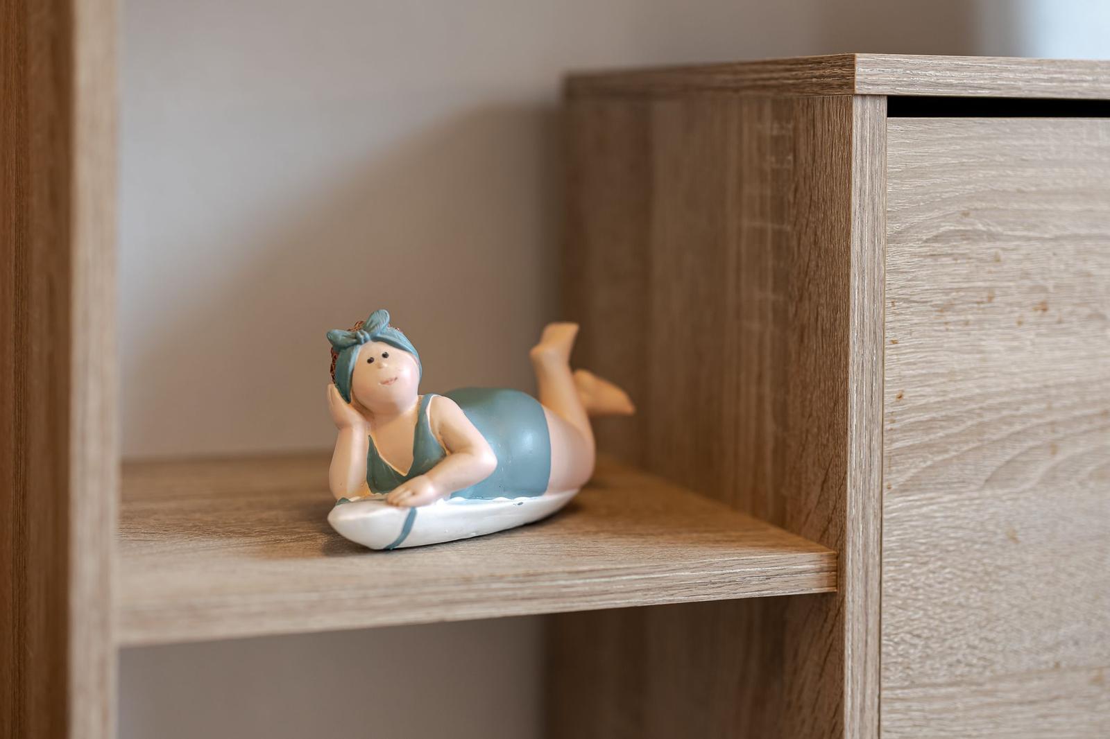 Eine kleine Figur liegt auf einem Brett auf einer Holzregalstufe.