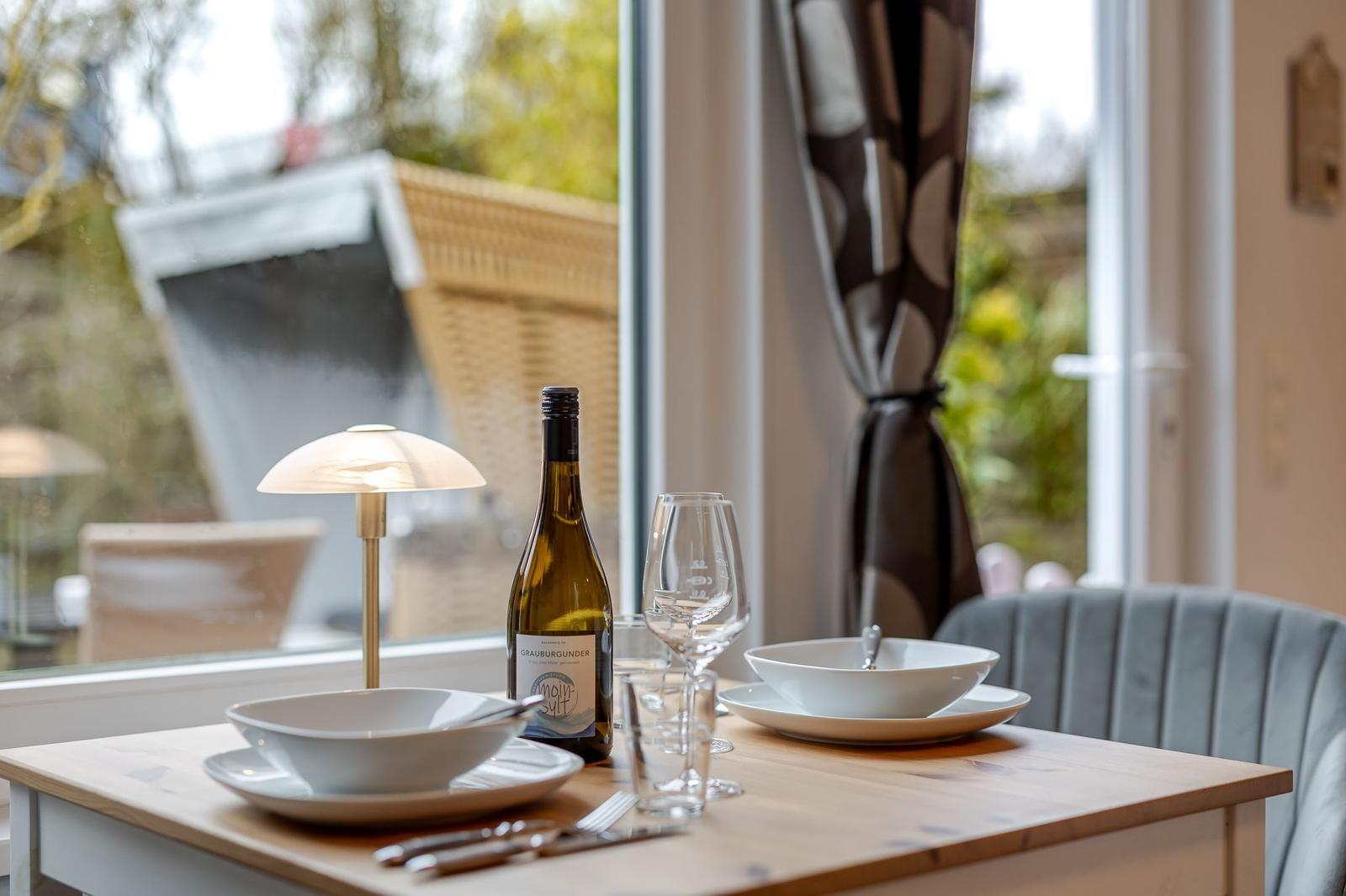 Esstisch mit Geschirr, Wein und Lampen vor Fenster mit Gartenblick.