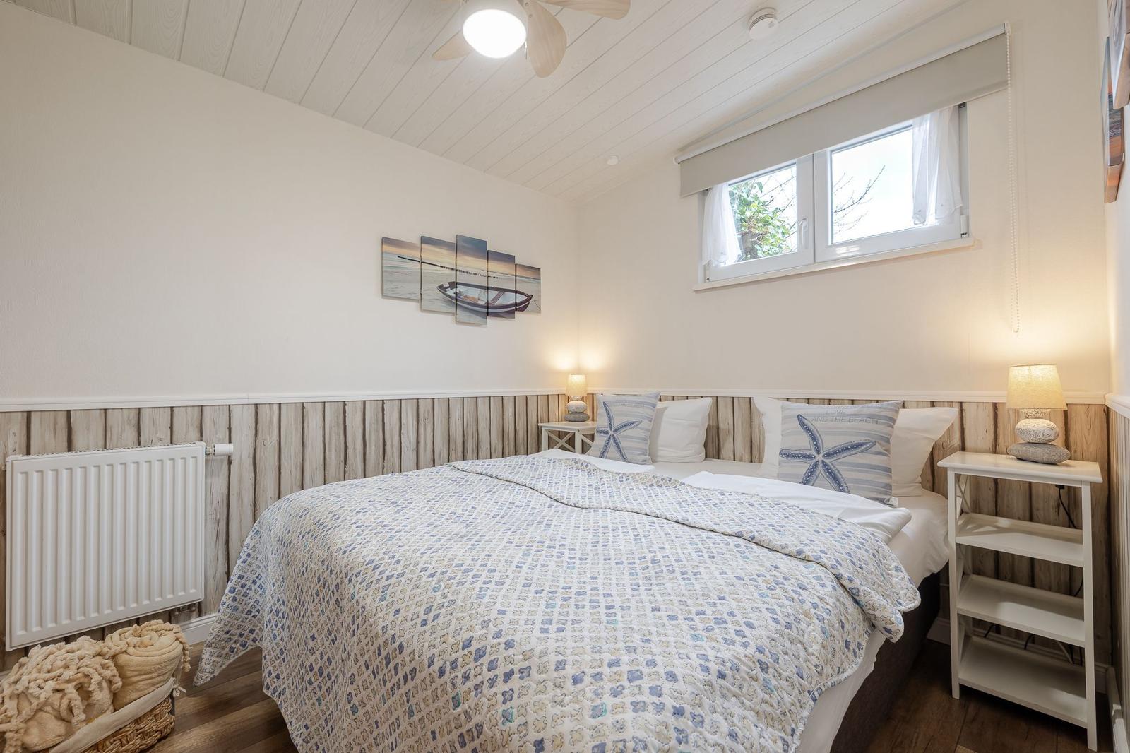 Schlafzimmer mit Bett, Nachttisch und Fenster. Wandgestaltung und Bettwäsche im Strandstil.