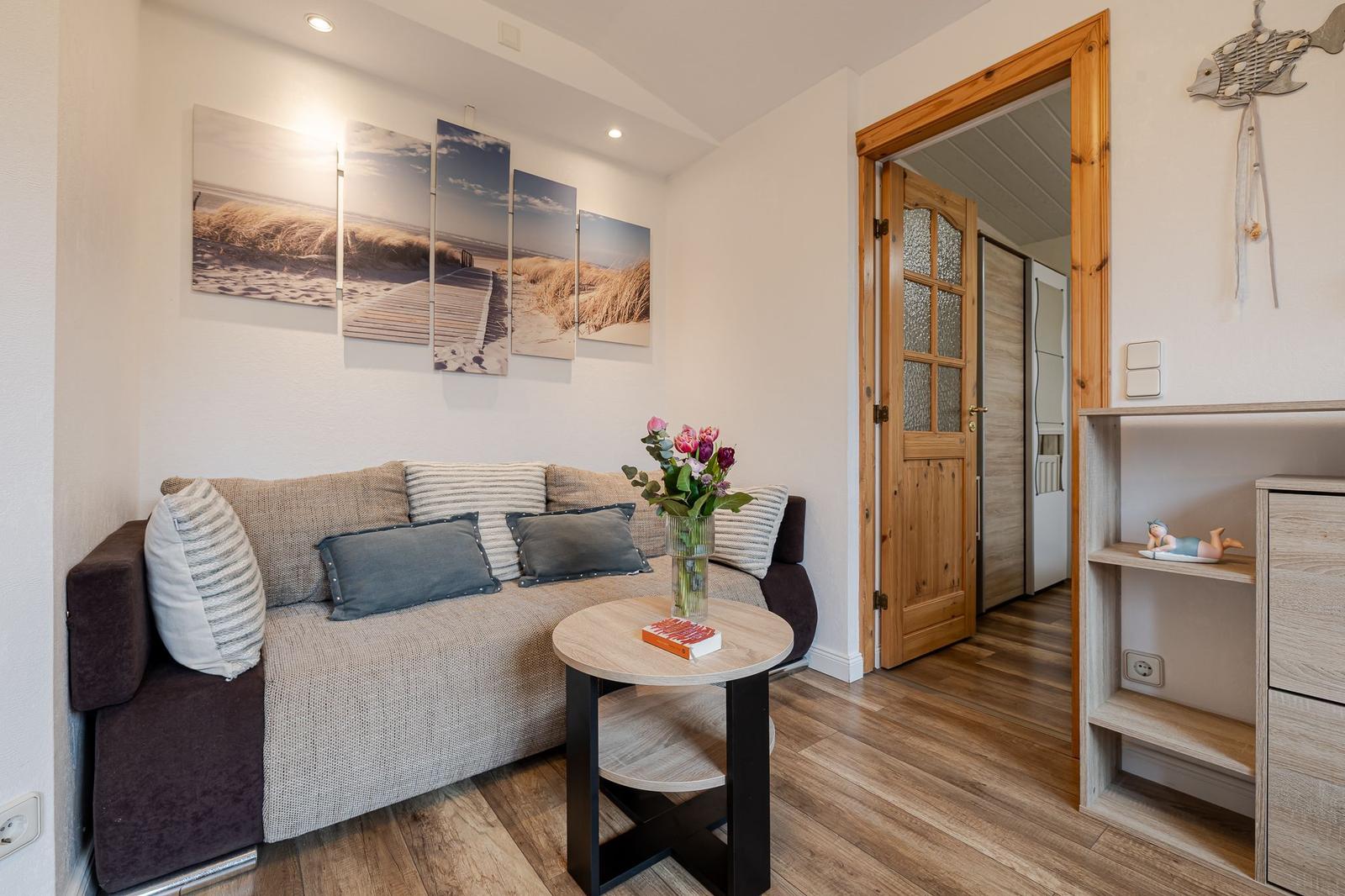 Wohnzimmer mit Sofa, Tisch und Wandbild. Holzfußboden und Tür zum Flur.