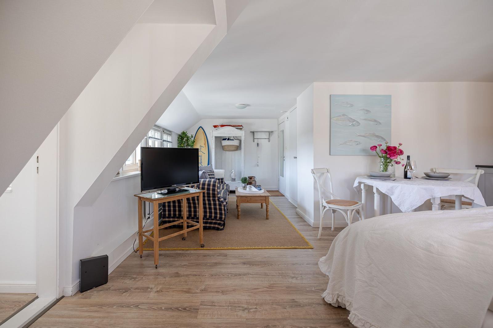 Living area with TV, dining table, and bed under sloped ceilings.