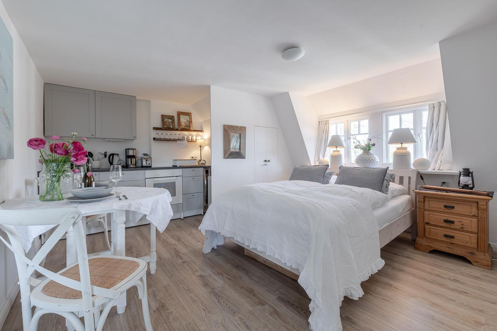 Bedroom with bed, nightstand, and windows. Kitchen area with table and chairs.