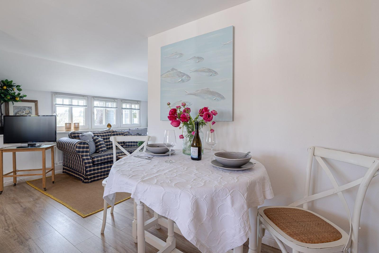 Dining table with tablecloth, flowers, and wine. Living area with sofa and TV.