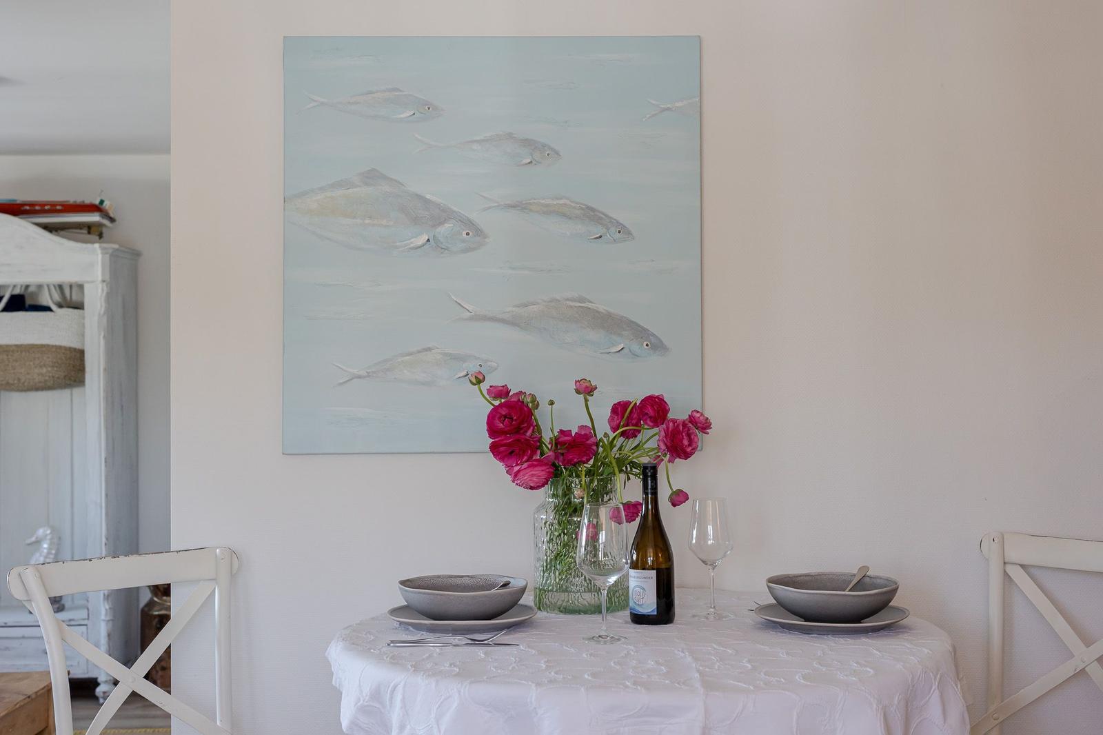 Dining table with tablecloth, two places, and wall painting with fish.