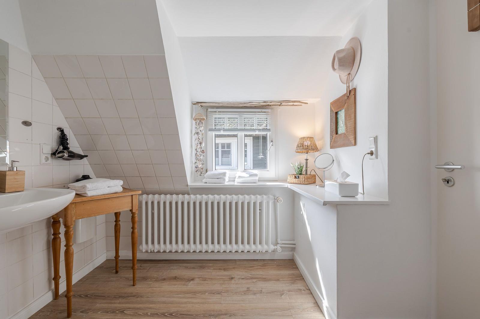 Bathroom with sloped ceiling, window, sink, and wooden table.