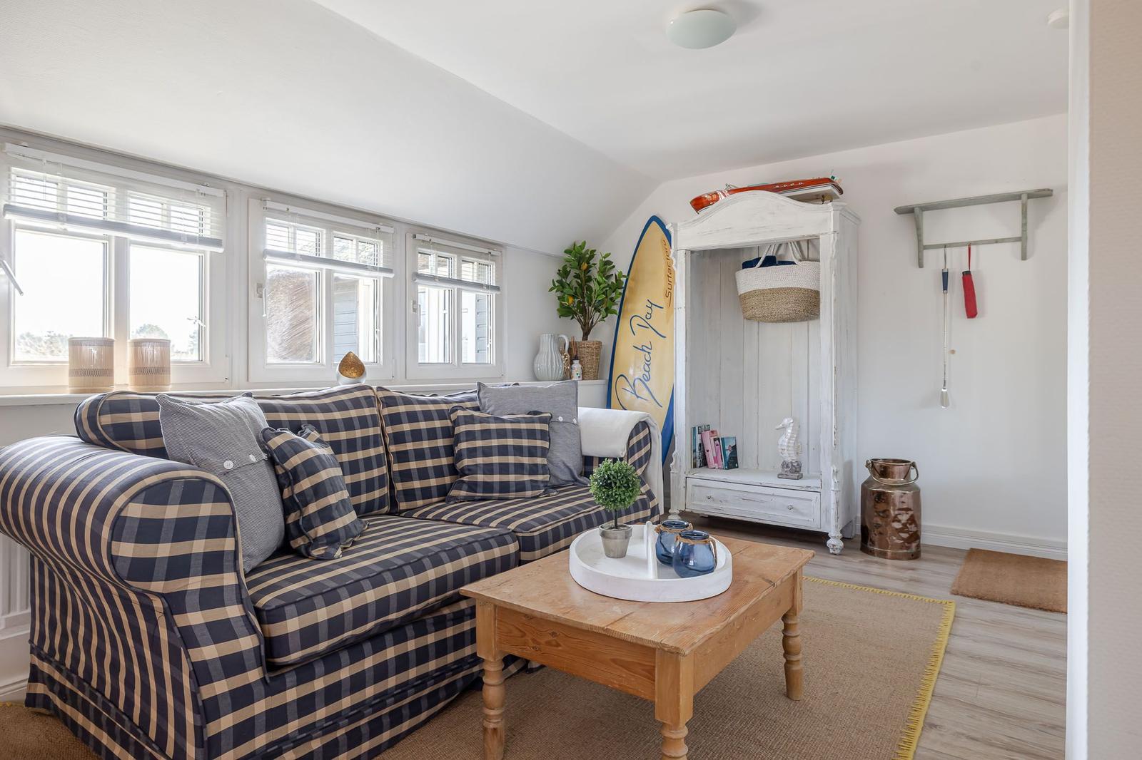 Living room with sofa, table, and wardrobe. Surfboard and plants are visible.