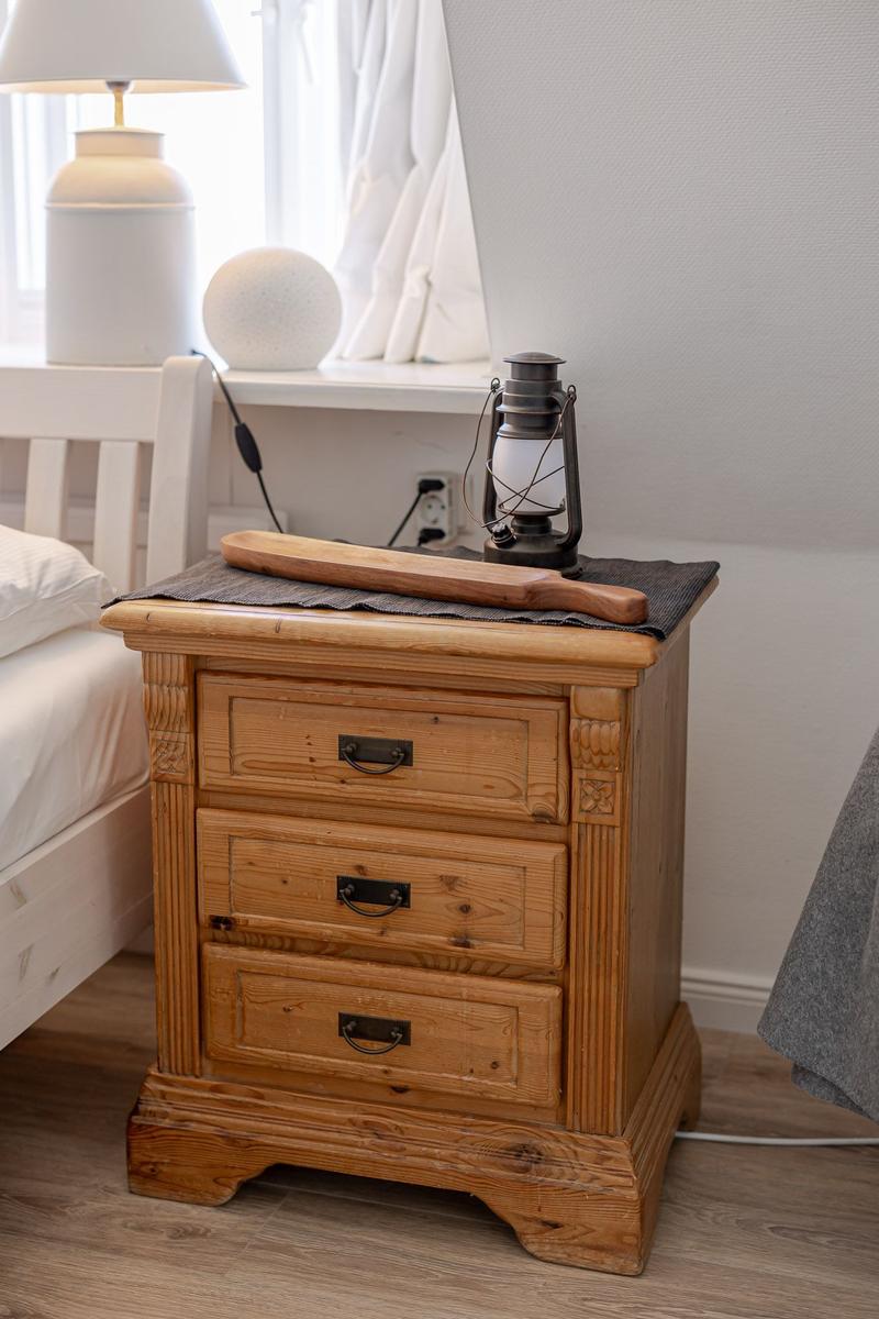 Wooden nightstand with three drawers, topped with lantern and wood piece.