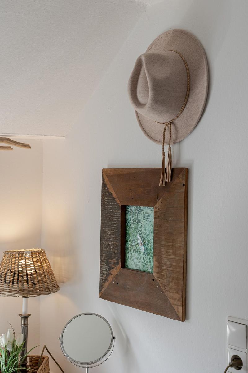 Hat hangs on wall next to wooden frame with picture and round mirror.