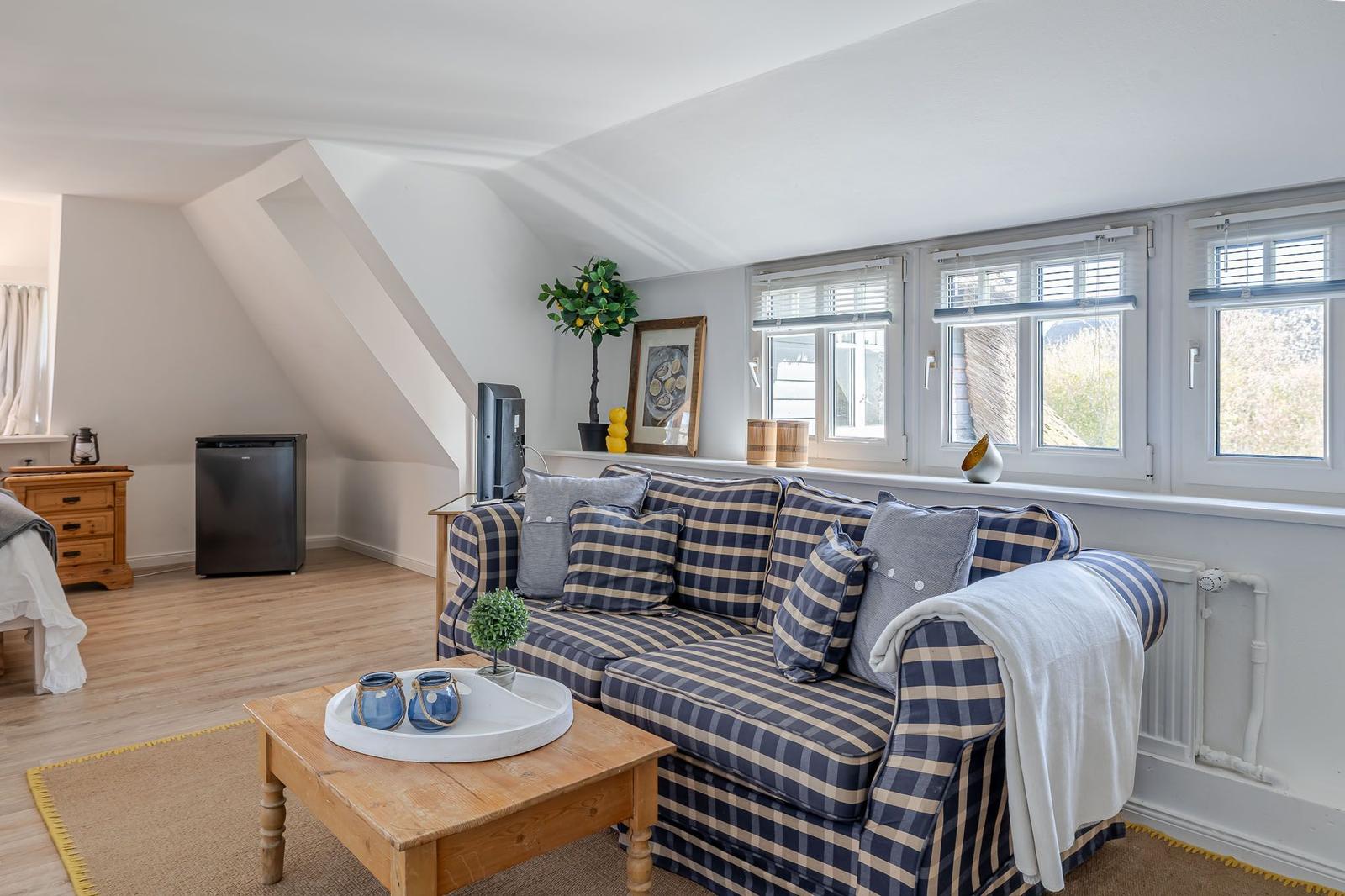 Living room with sofa, coffee table, and windows. Attic slope and wooden floor.