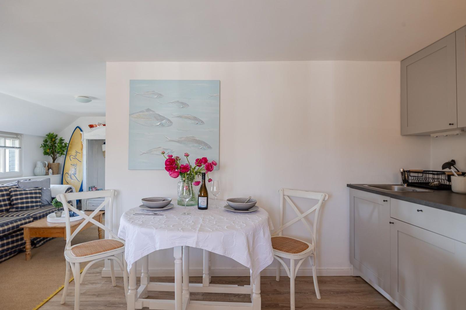 Dining area with table, chairs, and kitchenette. Wall art with fish and flowers on table.