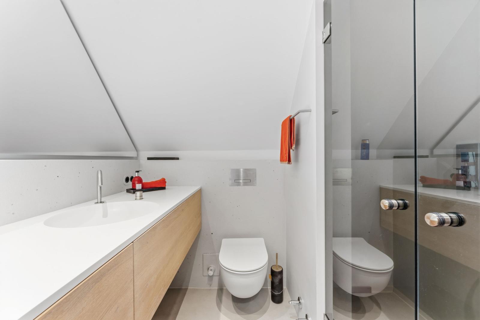 Badezimmer mit Waschbecken, Toilette und Dusche unter Dachschräge.