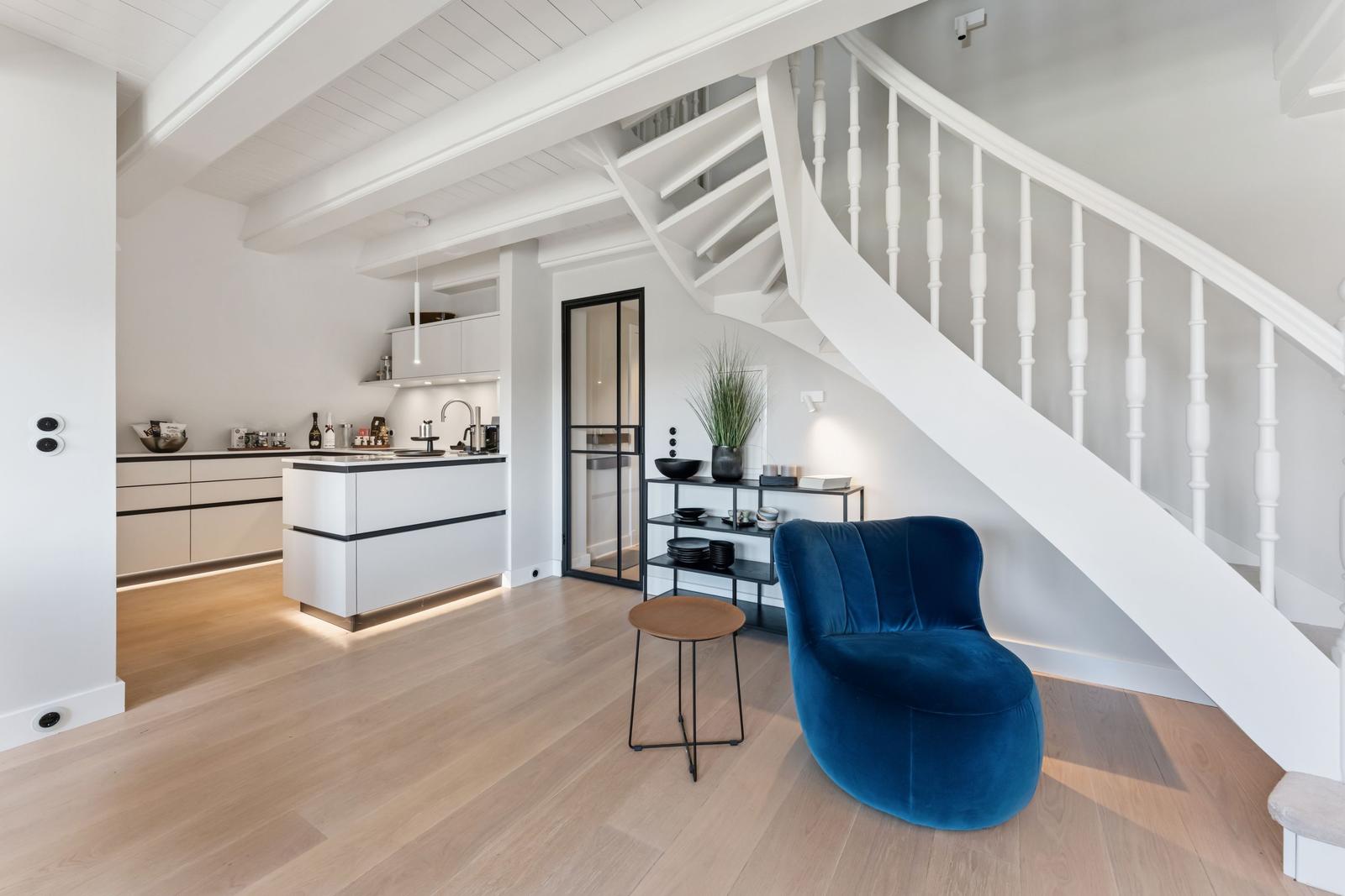 Moderne Küche mit weißen Schränken und blauer Sitzgelegenheit unter einer Treppe.