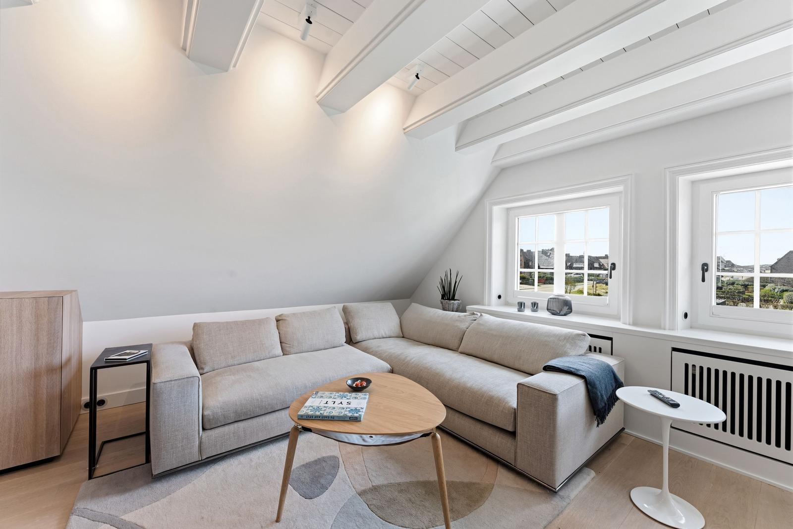 Wohnzimmer mit Ecksofa, Holztisch und Fenstern. Dachschrägen und helles Interieur.