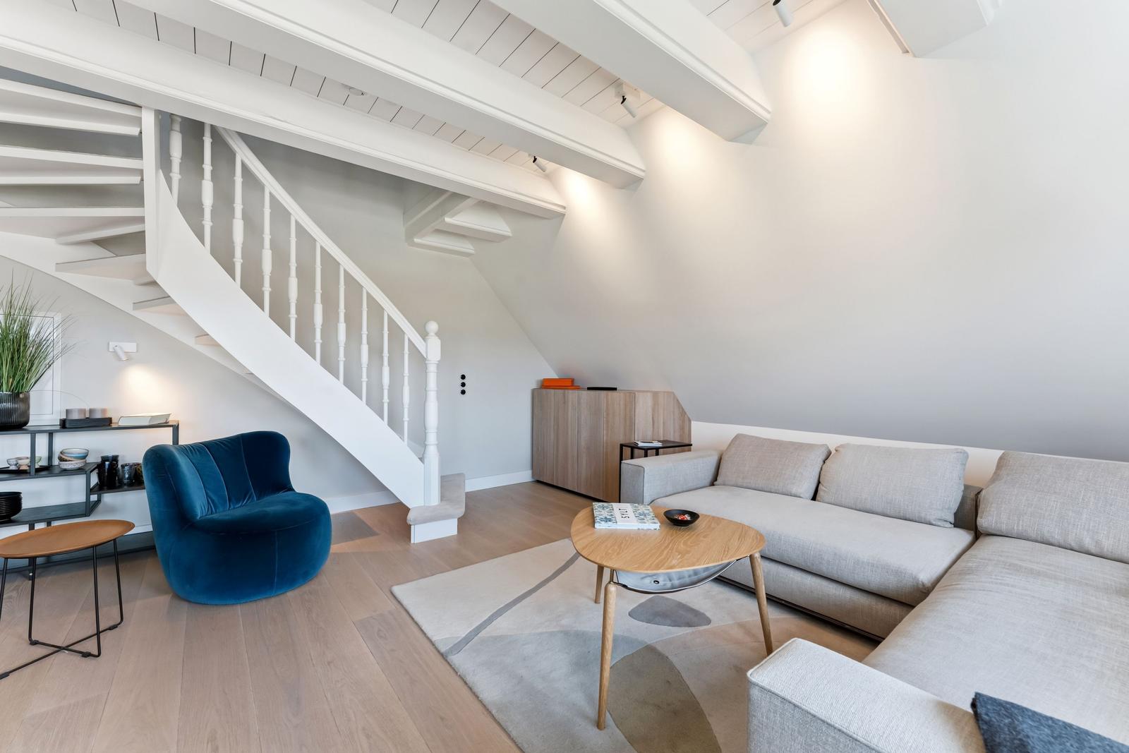 Wohnzimmer mit Sofa, blauer Sessel und weißer Treppe.