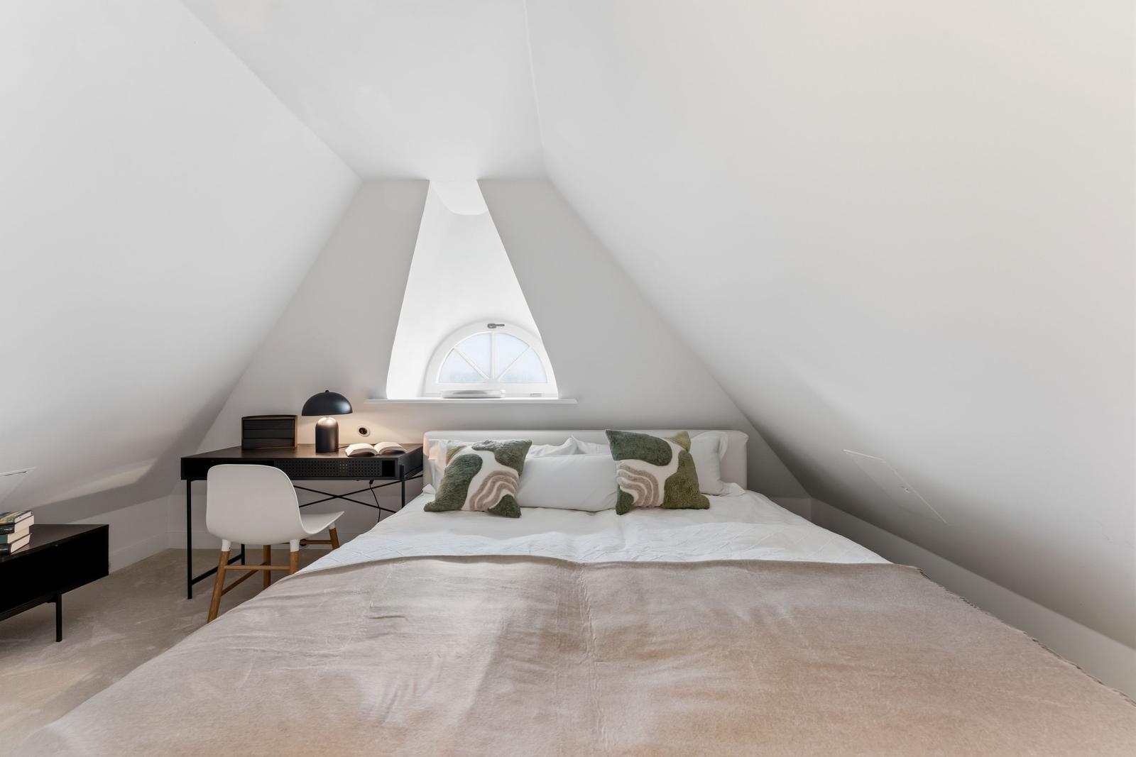Schlafzimmer mit Dachschräge, Bett, Schreibtisch und Fenster