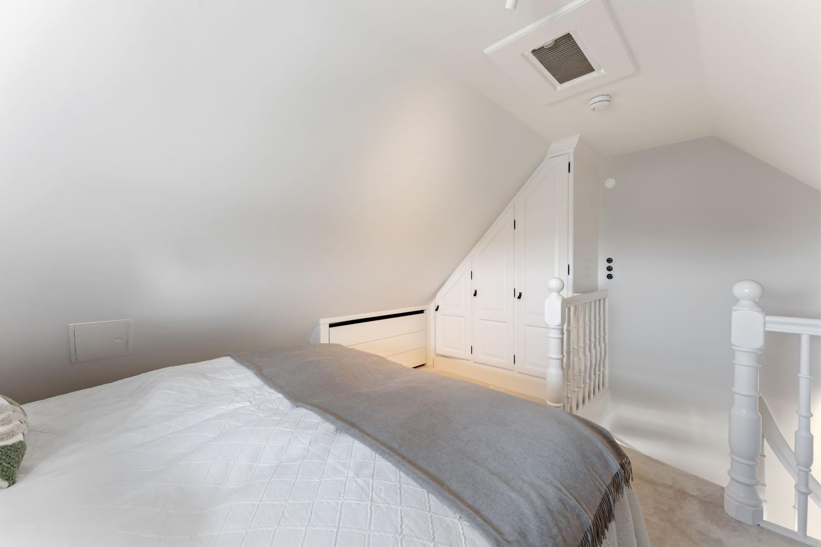 Schlafzimmer mit Dachschrägen, weißem Bett und Kleiderschrank