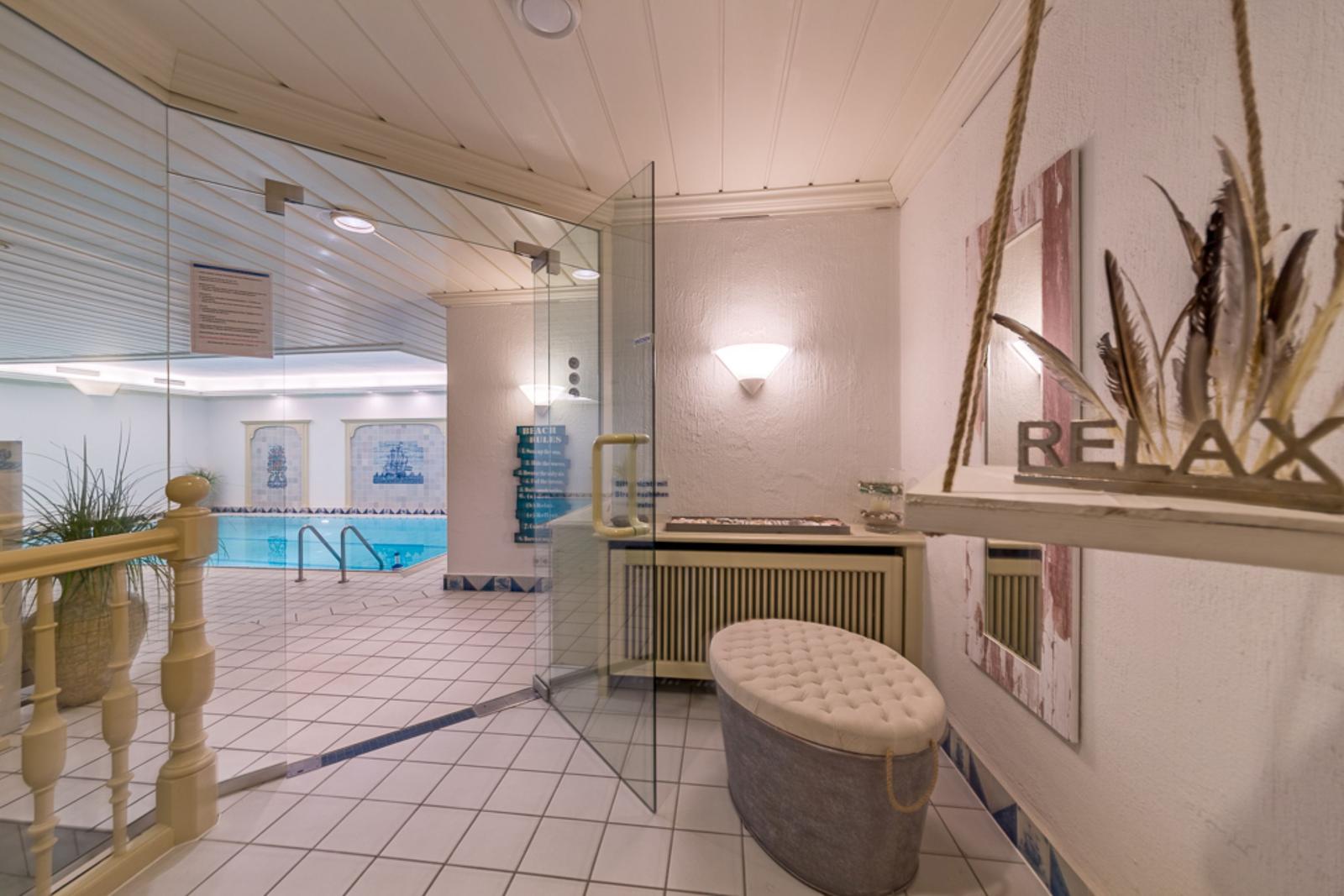 Indoorpoolbereich mit Glaswand, Sitzbank und Wanddekoration.
