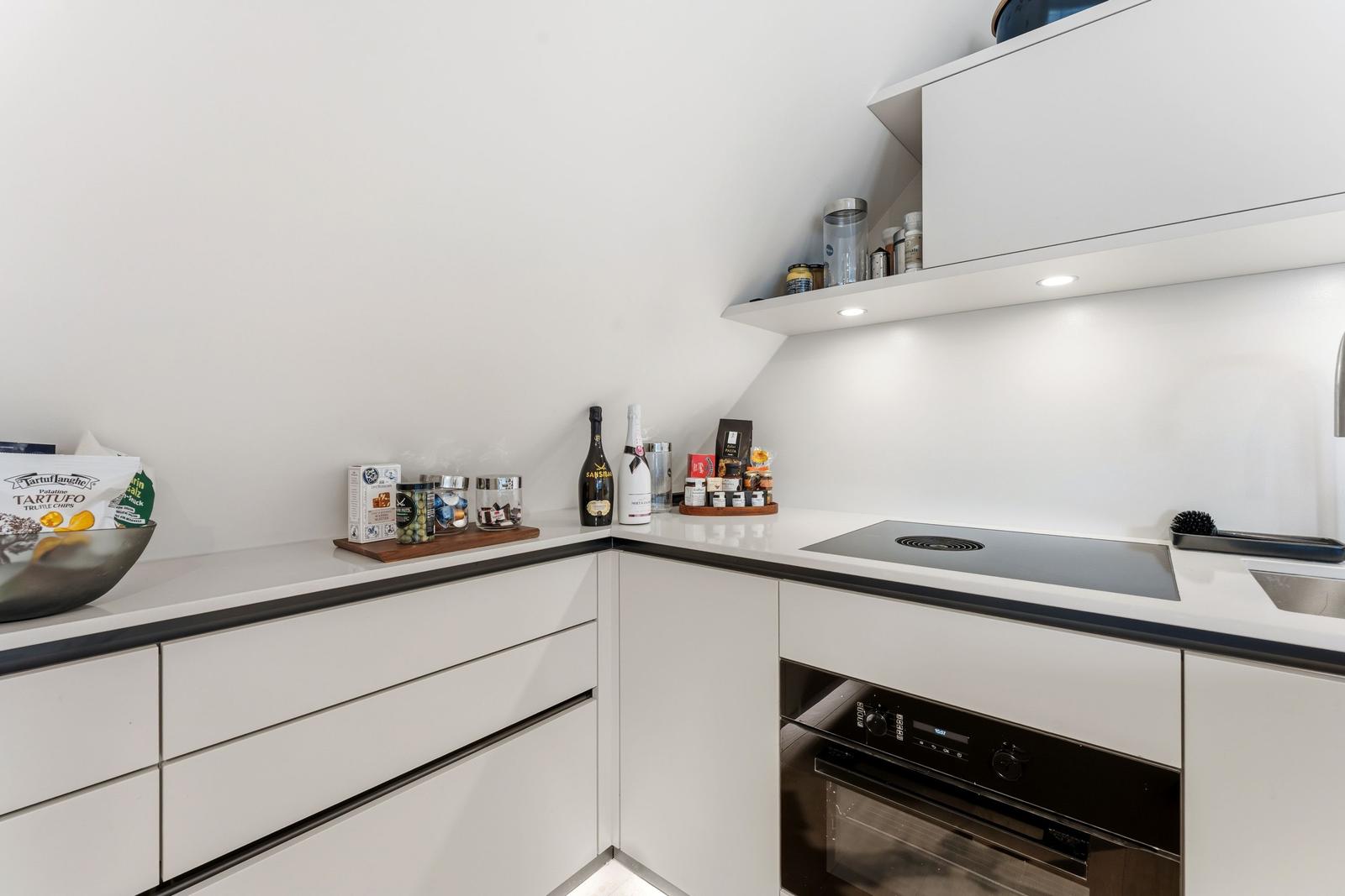 Moderne Küche mit weißen Schränken, Induktionskochfeld und integriertem Ofen.