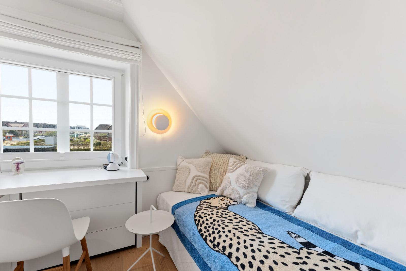 Schlafzimmer mit Dachschräge, Fenster, Bett und Schreibtisch.
