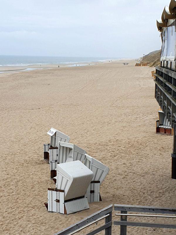 Strand mit weißen Strandkörben und Holzstegen. Blick auf den sandigen Strand und das Meer.
