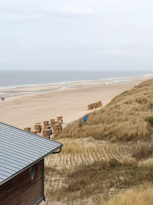 Blick auf Strand und Dünen mit Holzstühlen und Hausdach