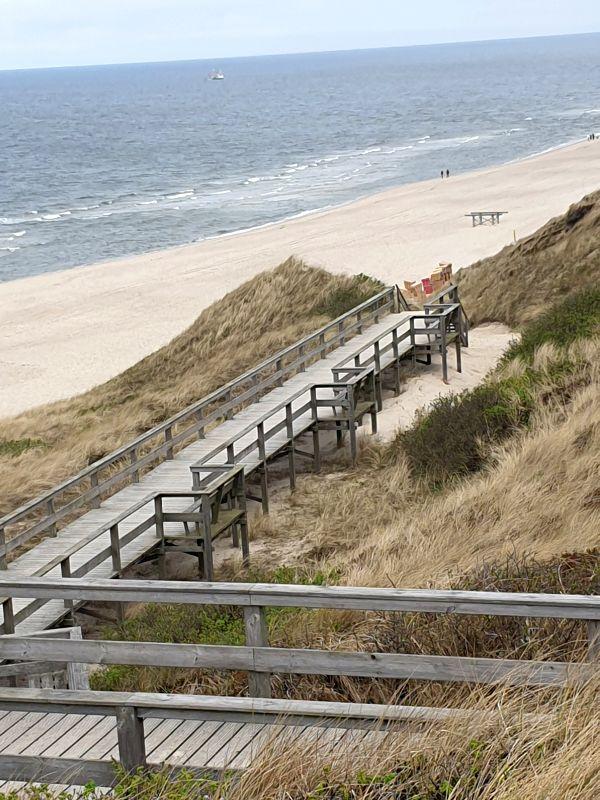 Holzsteg führt von Dünen zur Strandpromenade. Blick auf das Meer und Sandstrand.