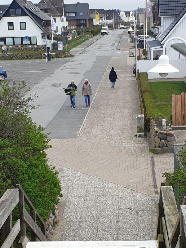 Drei Personen gehen auf einem gepflasterten Weg in einer Wohngegend entlang.