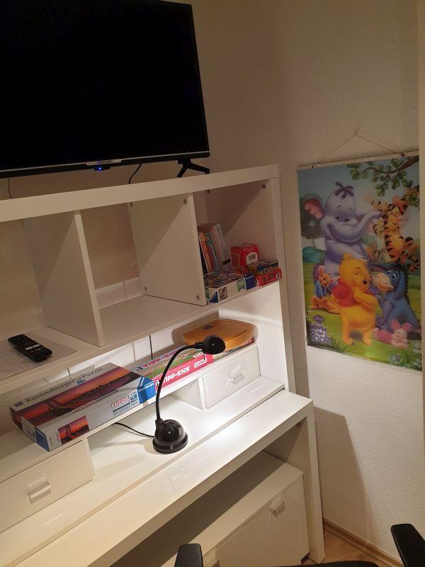 Schreibtisch mit Fernseher, Spielzeug und Kinderposter an der Wand.