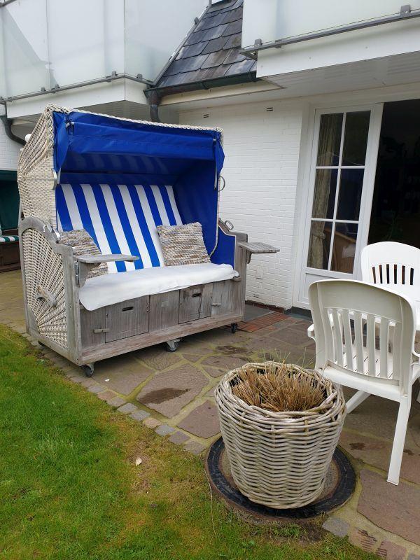 Terrasse mit Strandkorb, weißen Stühlen und Pflanzenkorb.
