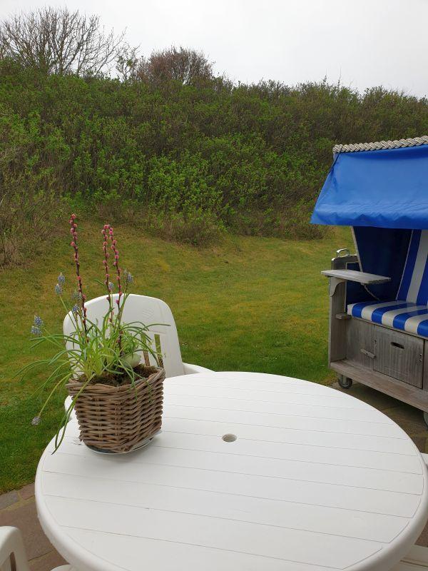 Runder Tisch mit Stuhl und Pflanze vor Strandkorb und Grünfläche.