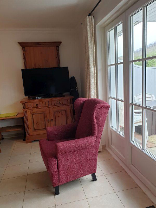 Ein Raum mit rotem Sessel, Fernseher und Fenster zur Terrasse.