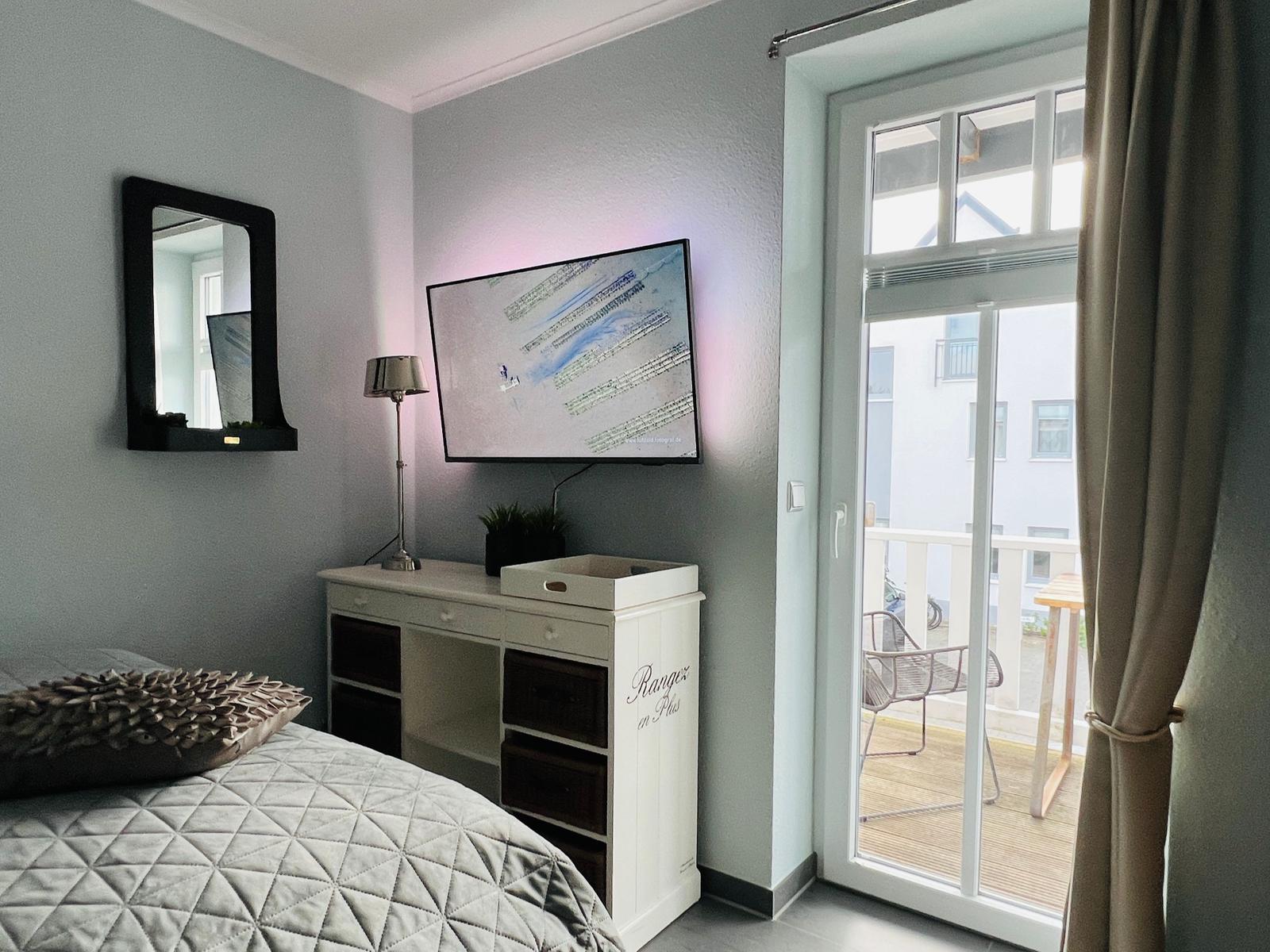 Zweites Schlafzimmer mit Flachbildfernseher und direktem Zugang zum West-Teakholzbalkon mit Strandkorb und hochwertigen Sitzmöbeln.