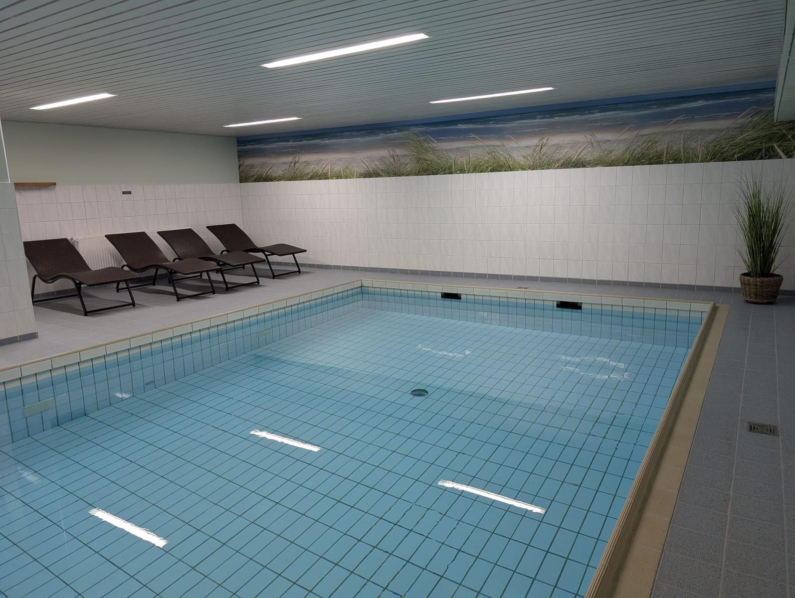 Innere Schwimmhalle mit Liegestühlen und Strandbildwand.