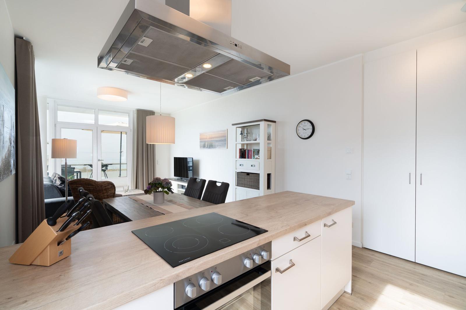 Küche mit Holzoberfläche und Induktionskochfeld. Essbereich und Wohnzimmer im Hintergrund.
