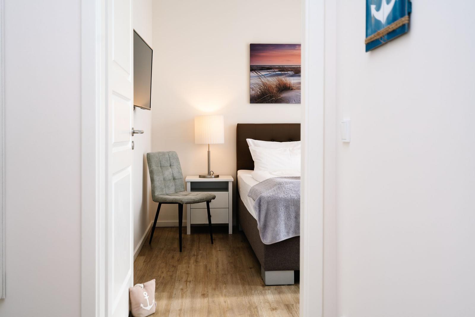 Schlafzimmer mit Bett, Nachttisch, Stuhl und Wandbild