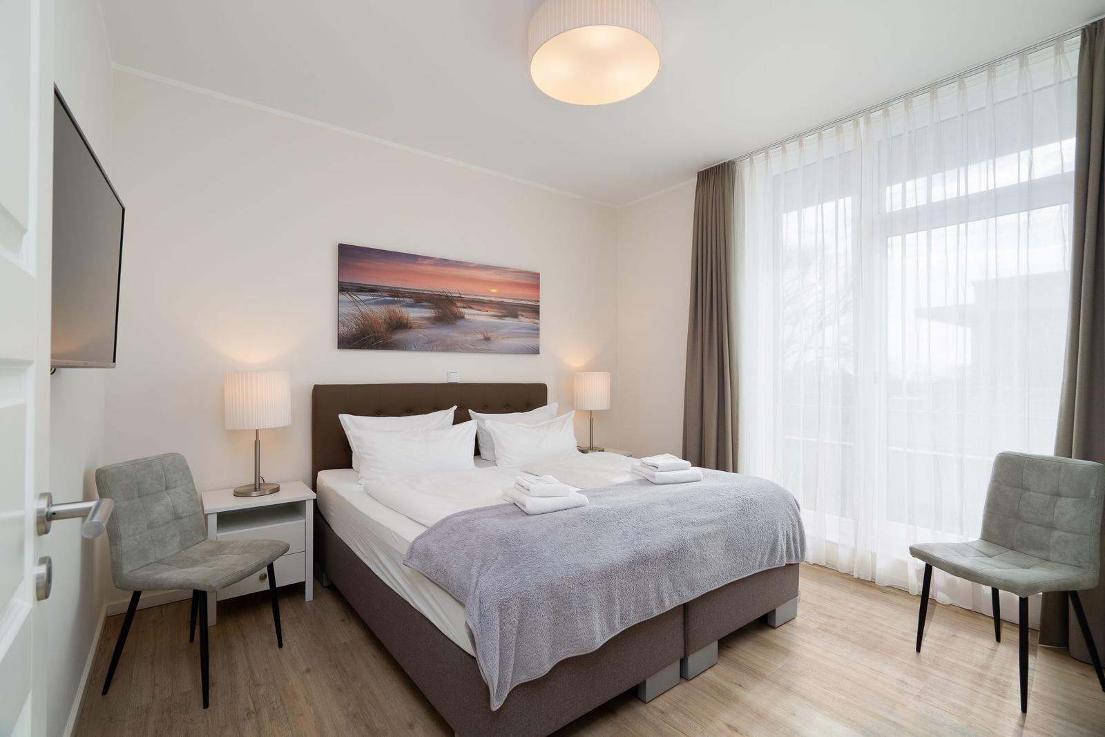 Schlafzimmer mit Bett, zwei Stühlen, Nachttischen und Wandbild.