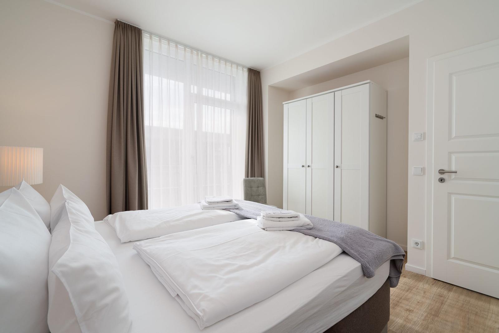 Schlafzimmer mit Bett, Kleiderschrank und Fenster mit Vorhängen.