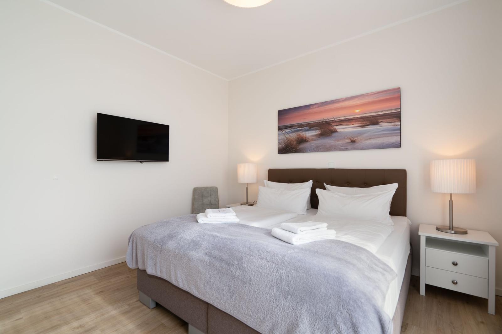 Schlafzimmer mit Doppelbett, Wandbild, Nachttisch und Fernseher.