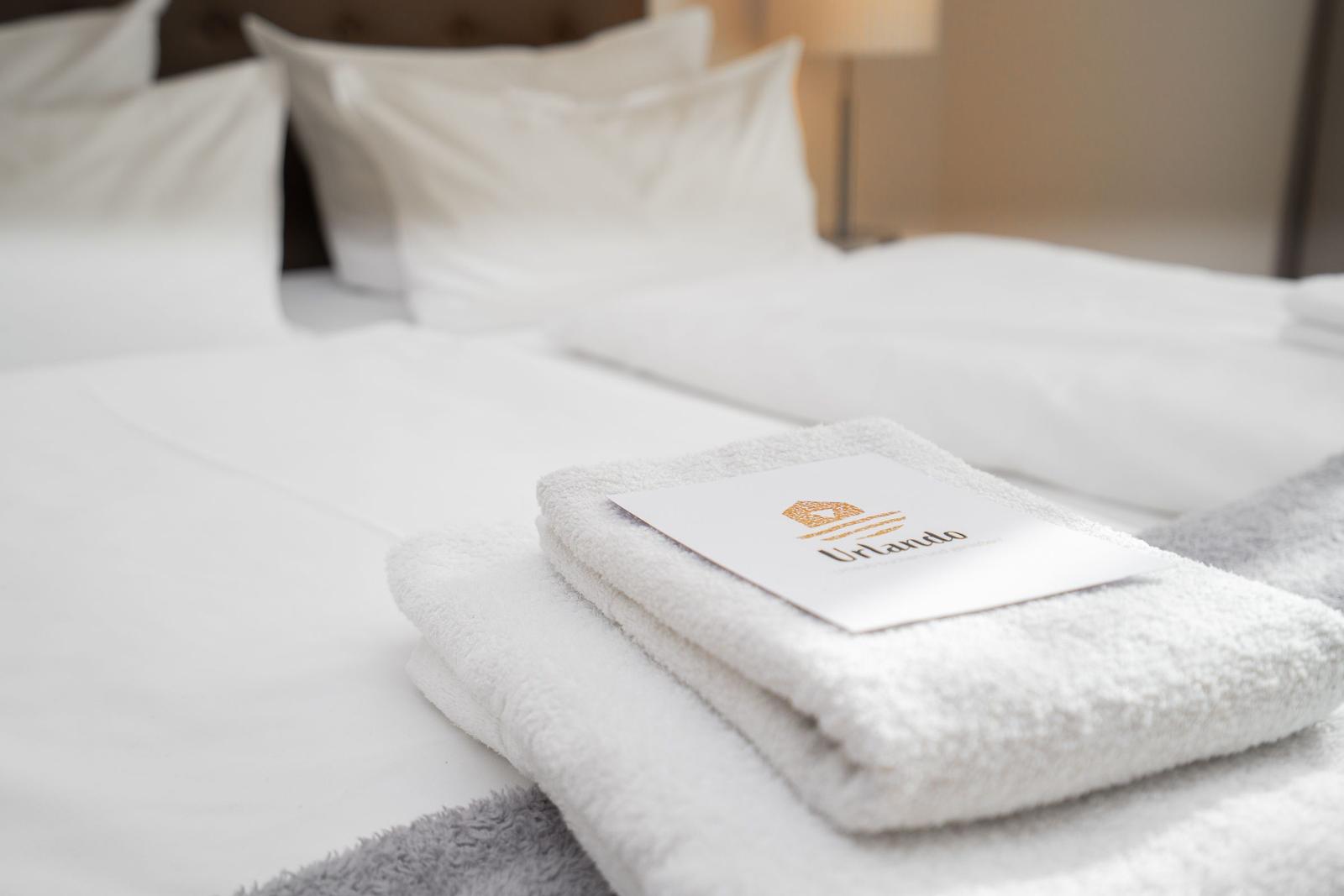 Bett mit weißen Laken und gefalteten Handtüchern mit Logo.
