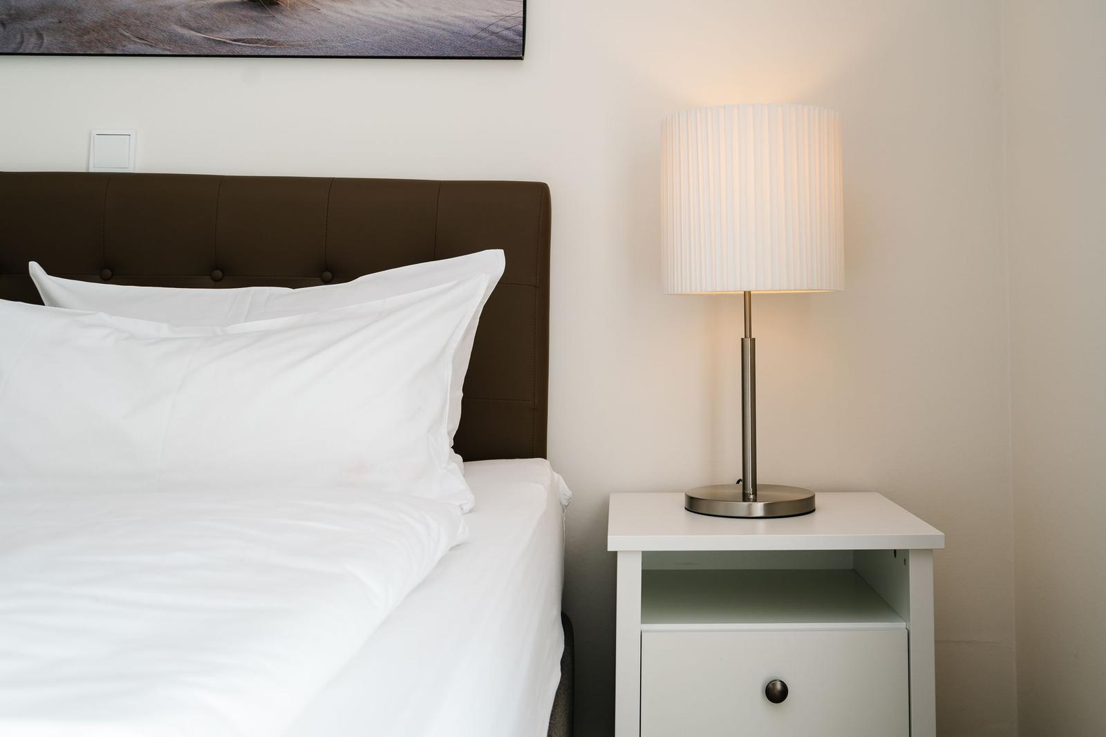 Schlafzimmer mit Bett, Nachttisch und Lampe. Wandbild über dem Kopfteil.