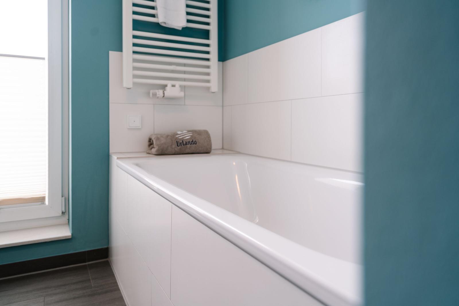 Bad mit Badewanne, Duschwand und Fenster mit Jalousie.