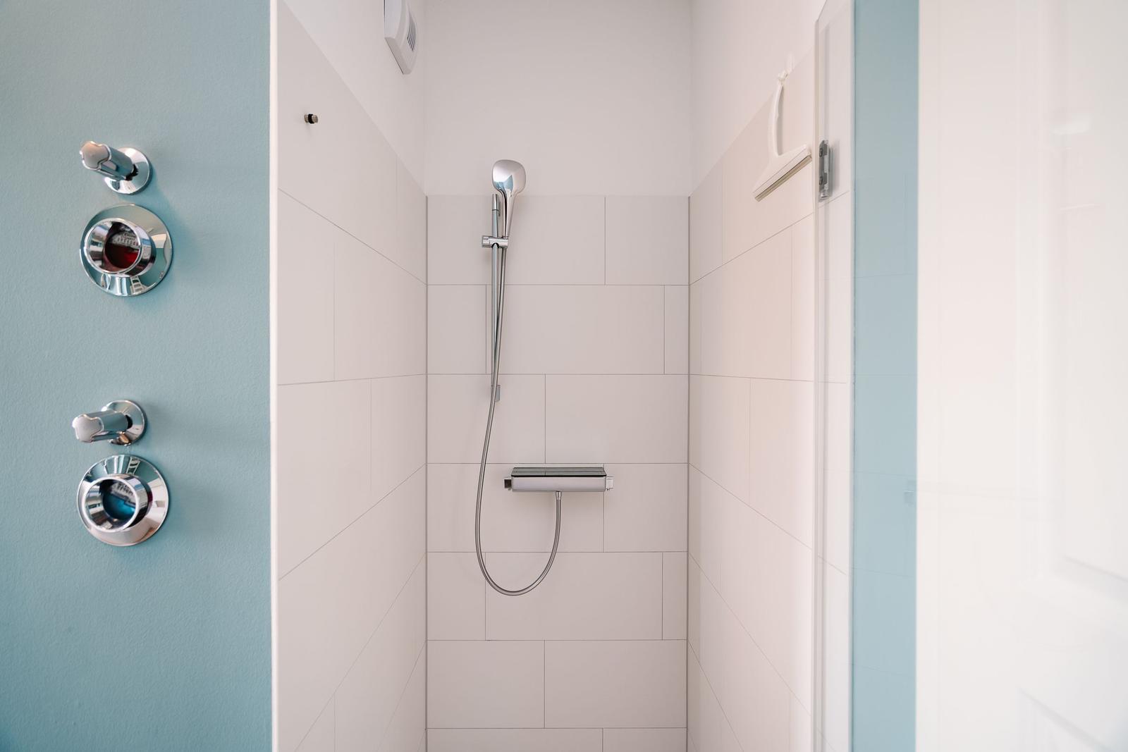Dusche mit Handbrause und Chromarmaturen an blauer Wand